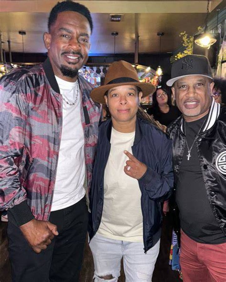 Chaunte Wayans wearing a cap and mike in her hand performs stand-up comedy in front of audience.