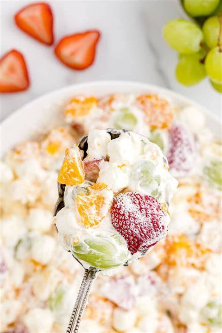 Fruit salad with pudding and white cream on a white plate with a gold fork.