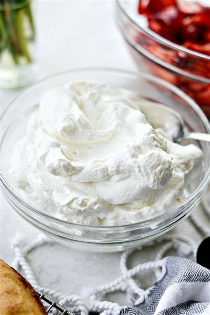 Homemade whipped cream in a red bowl with a stainless beater.