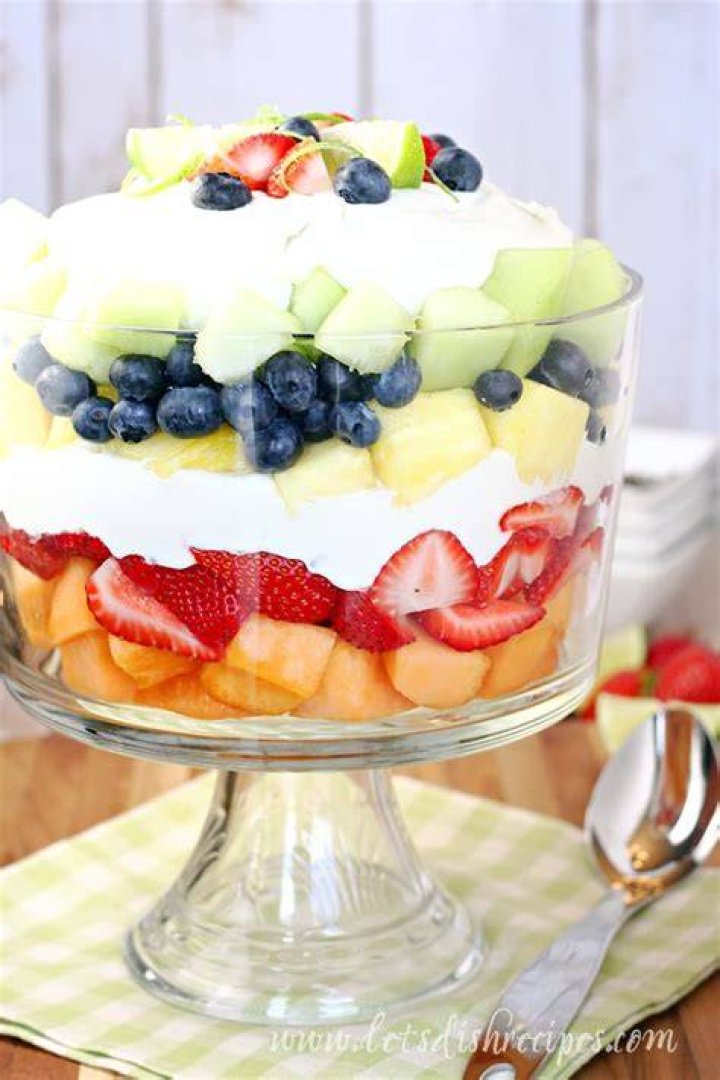 Layered fruit salad in a glass trifle dish with pudding on top.